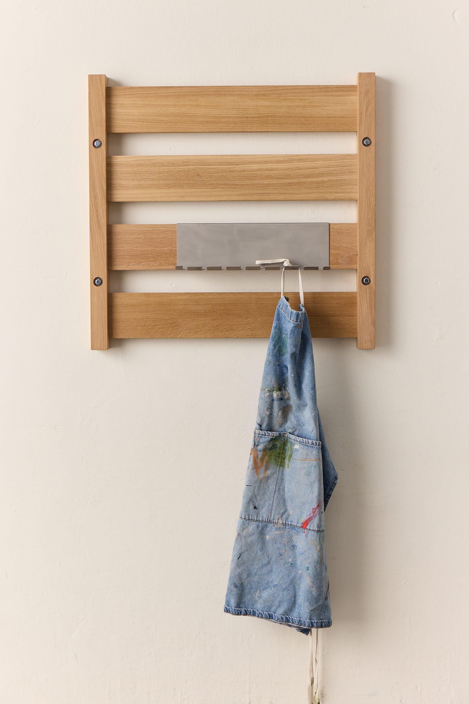 The Wall Wandmodul in Eiche mit Edelstahl-Ablage und Haken. Eine Arbeitsschürze hängt am Modul.